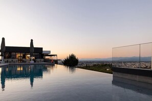 A modern infinity pool with a clear view of the cityscape and mountains in the background. - Ananti Resort & Spa (Trikala)