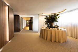 A hotel corridor with a round table set up for a meeting or event, flanked by wooden paneling and a carpeted floor. - Ananti Resort & Spa (Trikala)