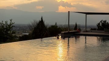 Una piscina infinita con vistas a montañas y un atardecer.