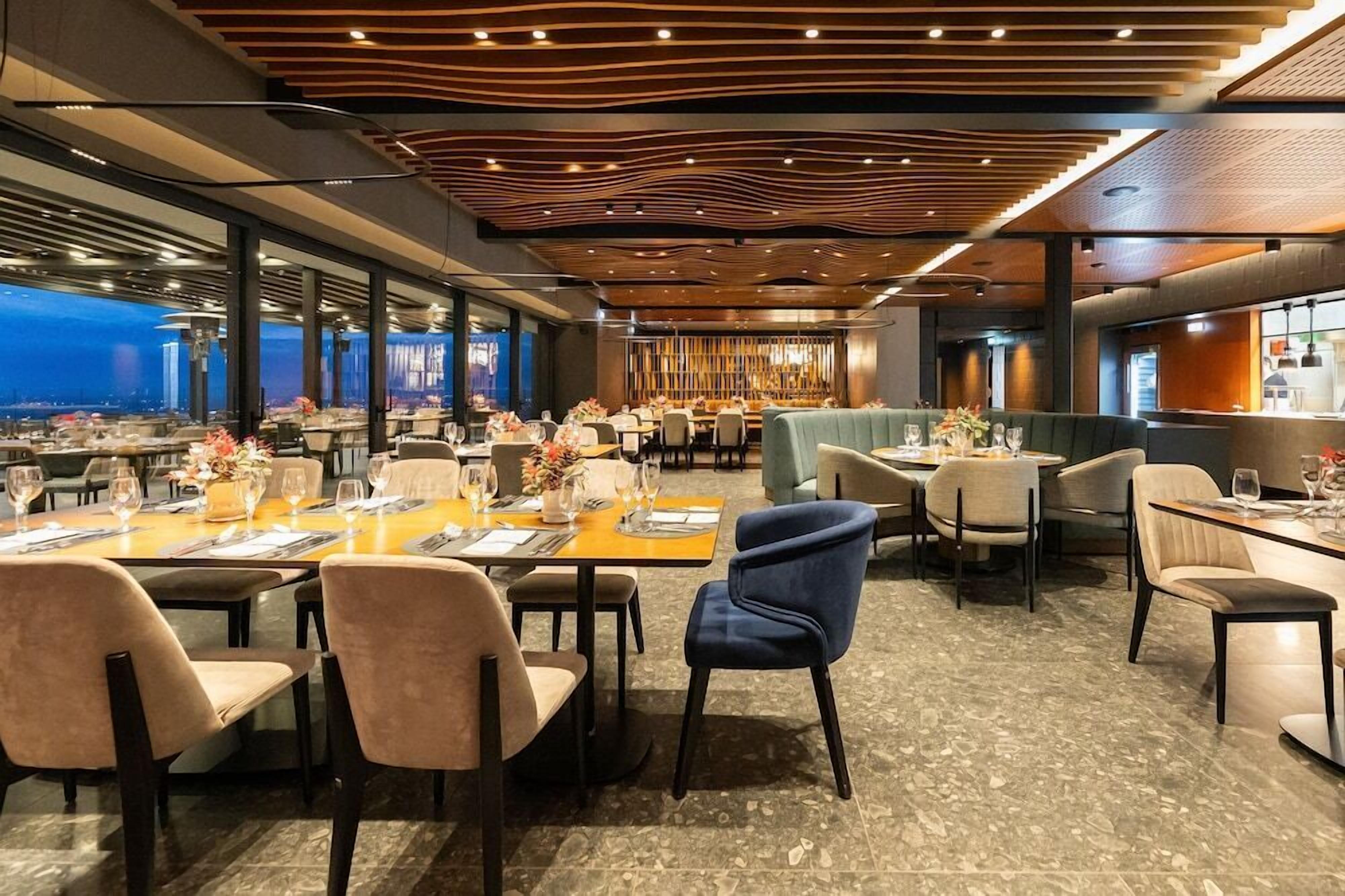 A restaurant with tables set for dining, a bar area, and a view of the cityscape.