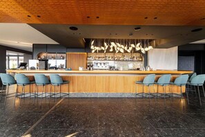Zona de bar moderna con mostrador de madera, taburetes y techo con lámparas colgantes.