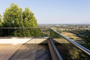 A rooftop terrace with a glass railing, offering a view of a green landscape and distant buildings. - Ananti Resort & Spa (Trikala)