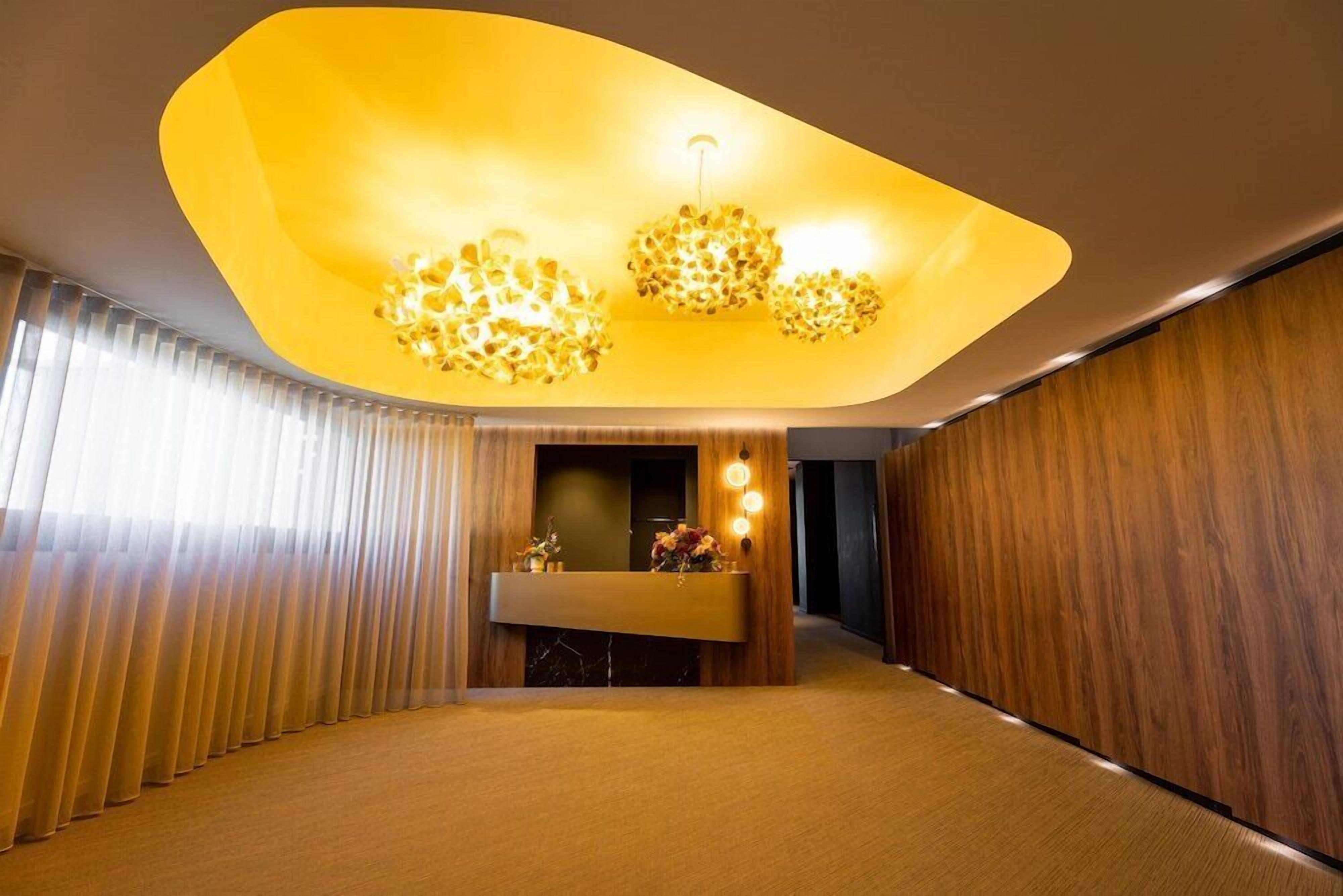 A modern interior with a reception desk, wooden paneling, and a unique ceiling light fixture.