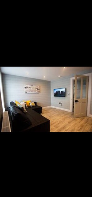 Un salon moderne avec un canapé noir, une table basse et un téléviseur à écran plat fixé au mur.