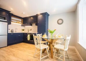 Une cuisine moderne avec des meubles de couleur bleu foncé, un plancher en bois et une table ronde entourée de chaises.