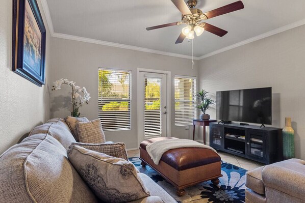 A living room with a sofa, ottoman, TV, and ceiling fan.