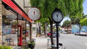 A street view with outdoor seating, a clock, and storefronts including a wine shop.