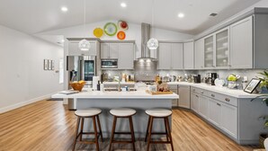 A modern kitchen with a central island, bar stools, stainless steel appliances, and pendant lighting.