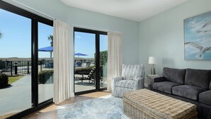 A spacious living room with a large sliding glass door leading to a balcony, a wicker ottoman, a grey sofa, and a striped armchair. - Phoenix VI 6013 Few Steps to Pool & Beach! (Orange Beach)