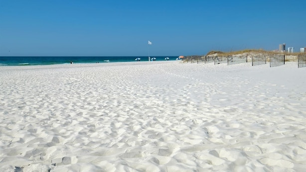 A wide, white sandy beach with a clear blue sky and calm sea. - Phoenix VI 6013 Few Steps to Pool & Beach! (Orange Beach)