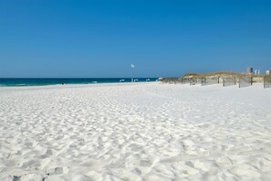 Uma extensa praia de areia branca, com céu azul límpido e mar calmo.