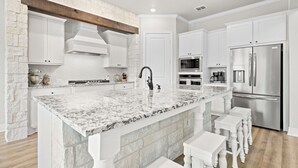 Una cucina moderna con mobili bianchi, un'isola in granito, elettrodomestici in acciaio inossidabile e travi in legno.