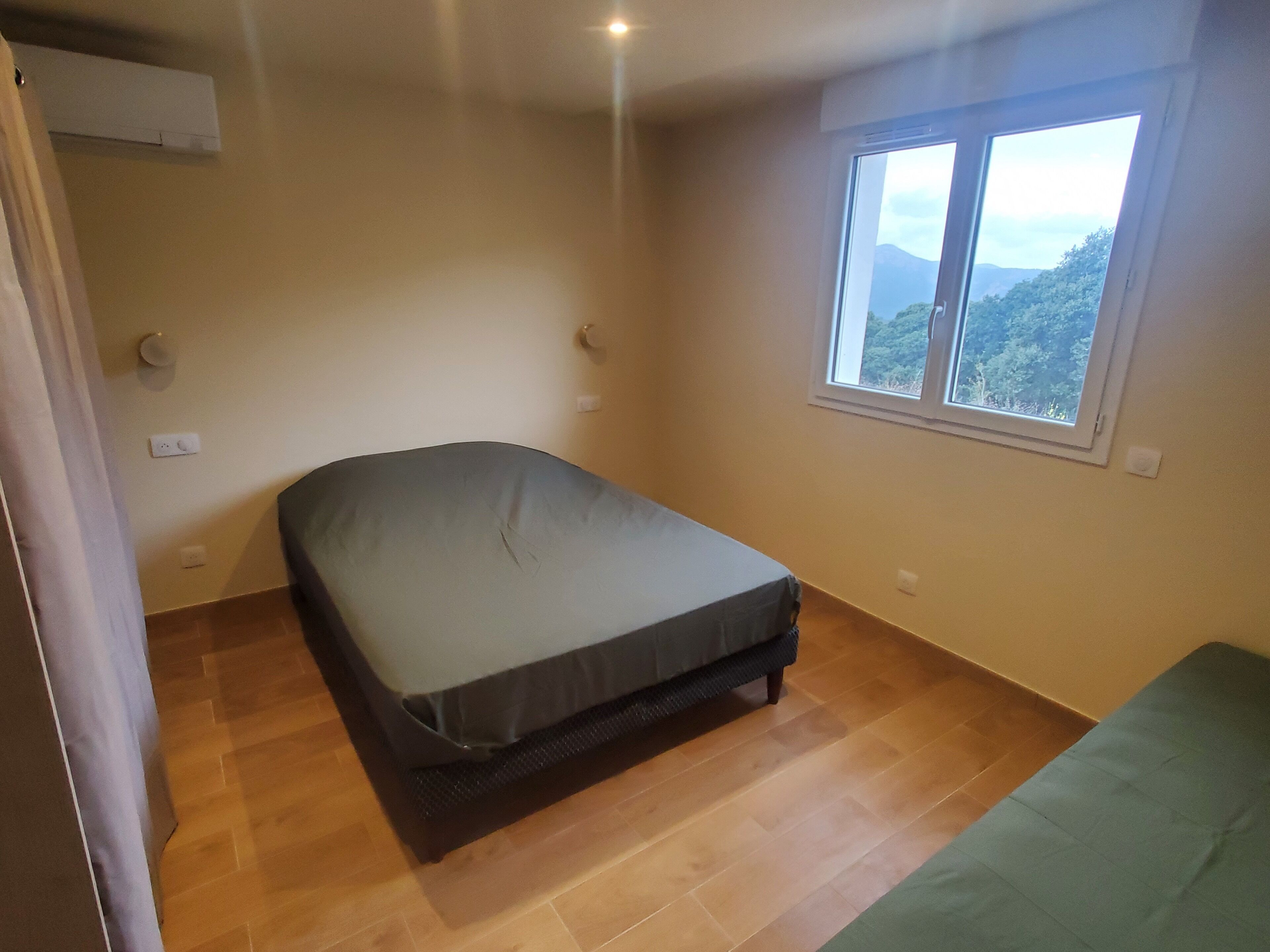 Ein kleines Zimmer mit einem Einzelbett und einem Fenster mit Blick auf Grünflächen und Berge.