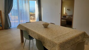 Una zona de menjador amb una taula preparada per a dues persones, vistes a l'exterior i una zona d'estar acollidora amb un sofà i coixins.