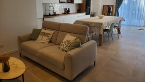 Un saló amb un sofà beix, una taula rodona petita amb un vas i una zona de menjador amb taula i cadires.