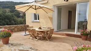 Un pati exterior amb una taula rodona i cadires, un ombrell gran i plantes en testos.
