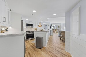 A modern kitchen with white cabinetry, a central island, stainless steel appliances, and a wooden floor.