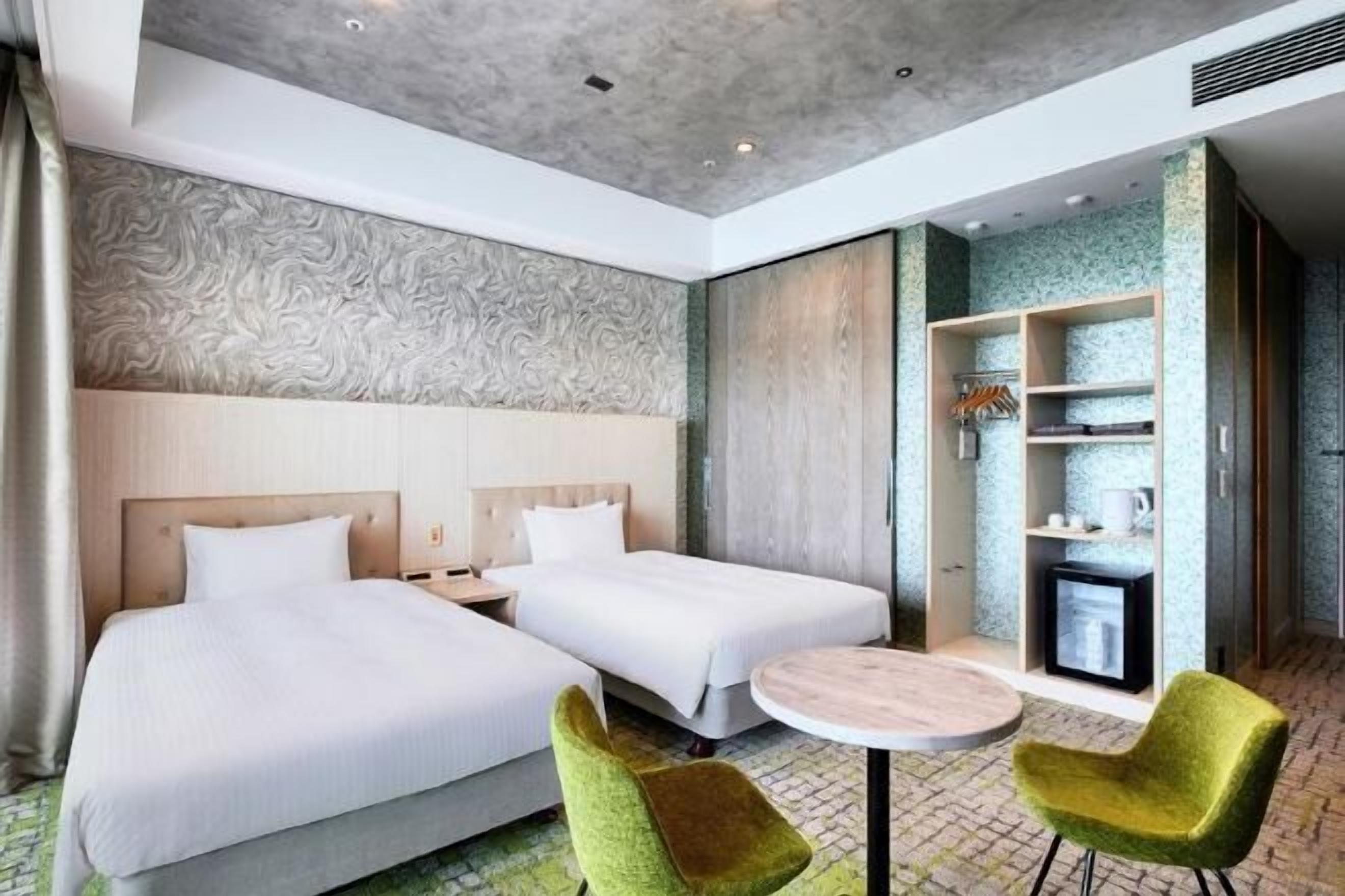 A hotel room with two beds, a small round table, and two green chairs.