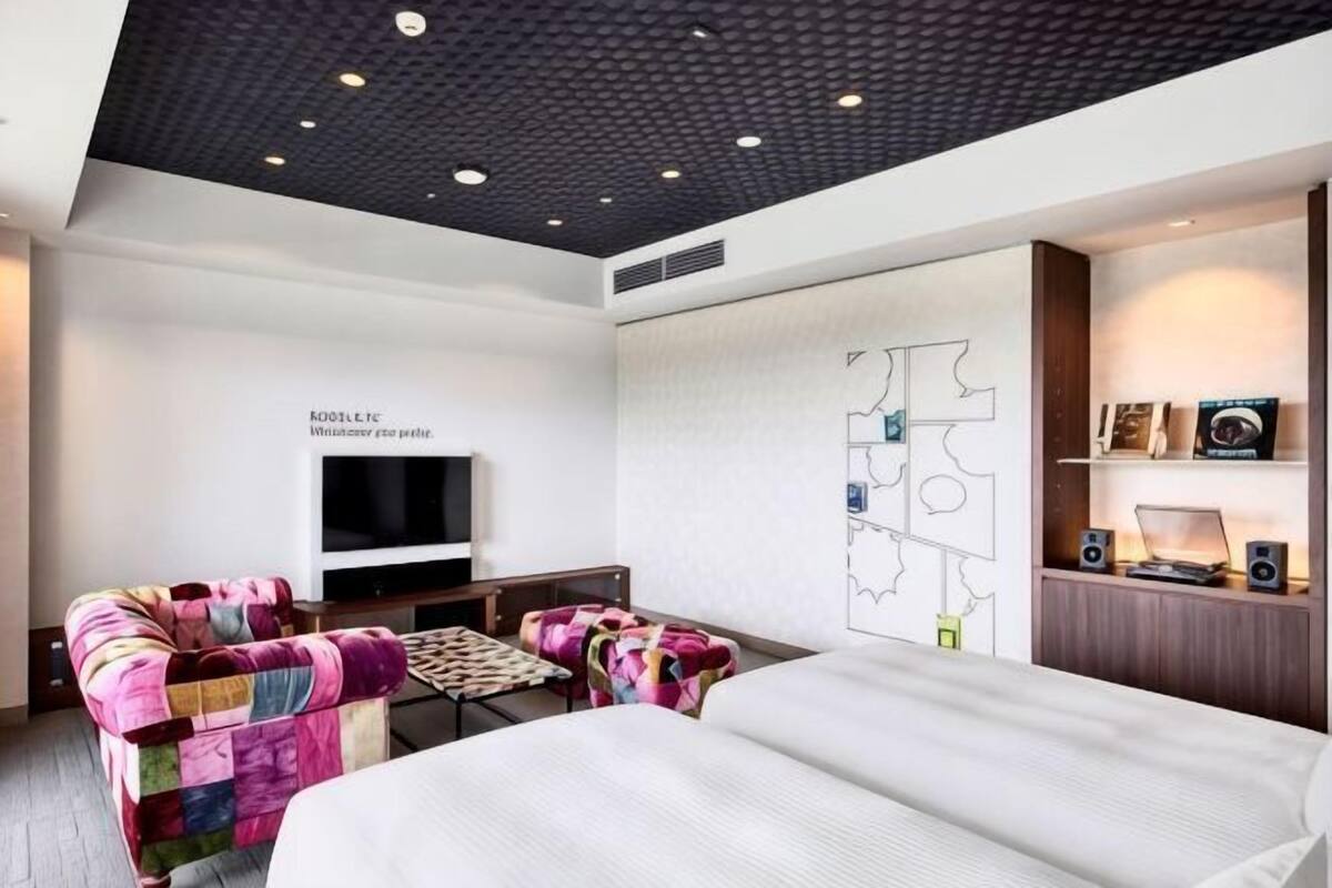 Una camera d'albergo moderna con un letto, una poltrona, una TV e una mappa appesa al muro.