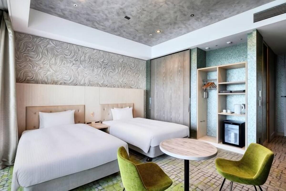 Una camera d'albergo con due letti, una televisione, un tavolino e una sedia verde.