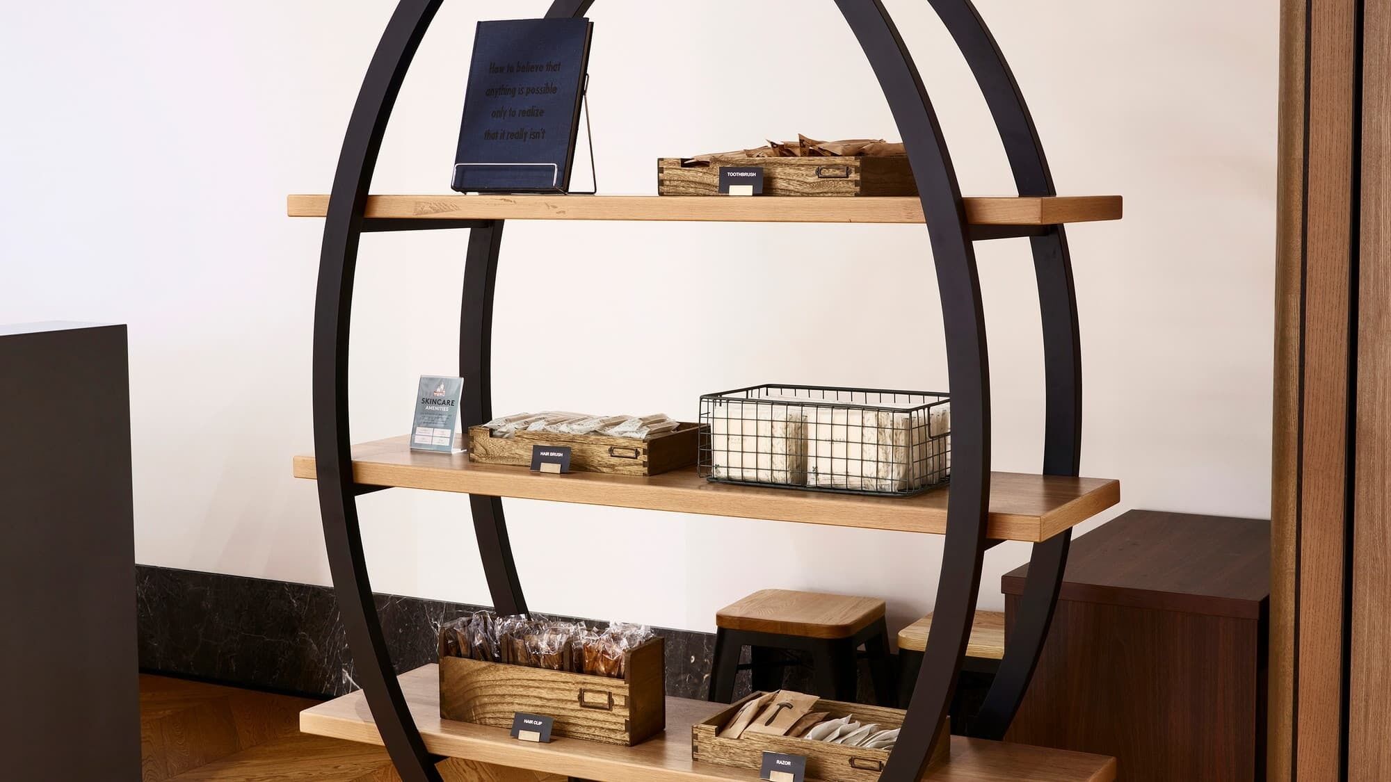 A multi-tiered wooden shelf with various items including a book, a toothbrush holder, a skincare product, and a metal basket.