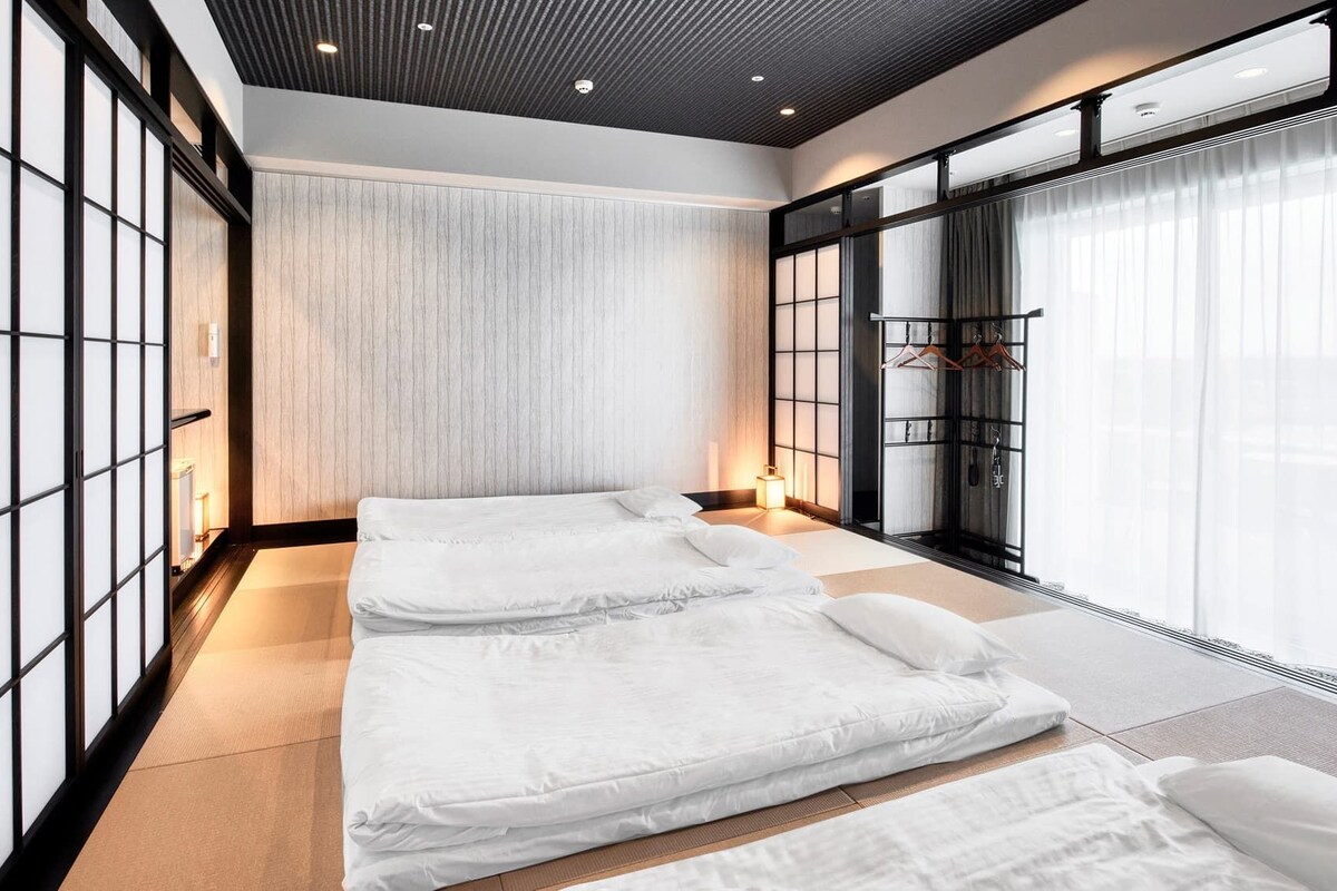 A modern room with a large bed, a wall-mounted TV, and a large window with curtains.