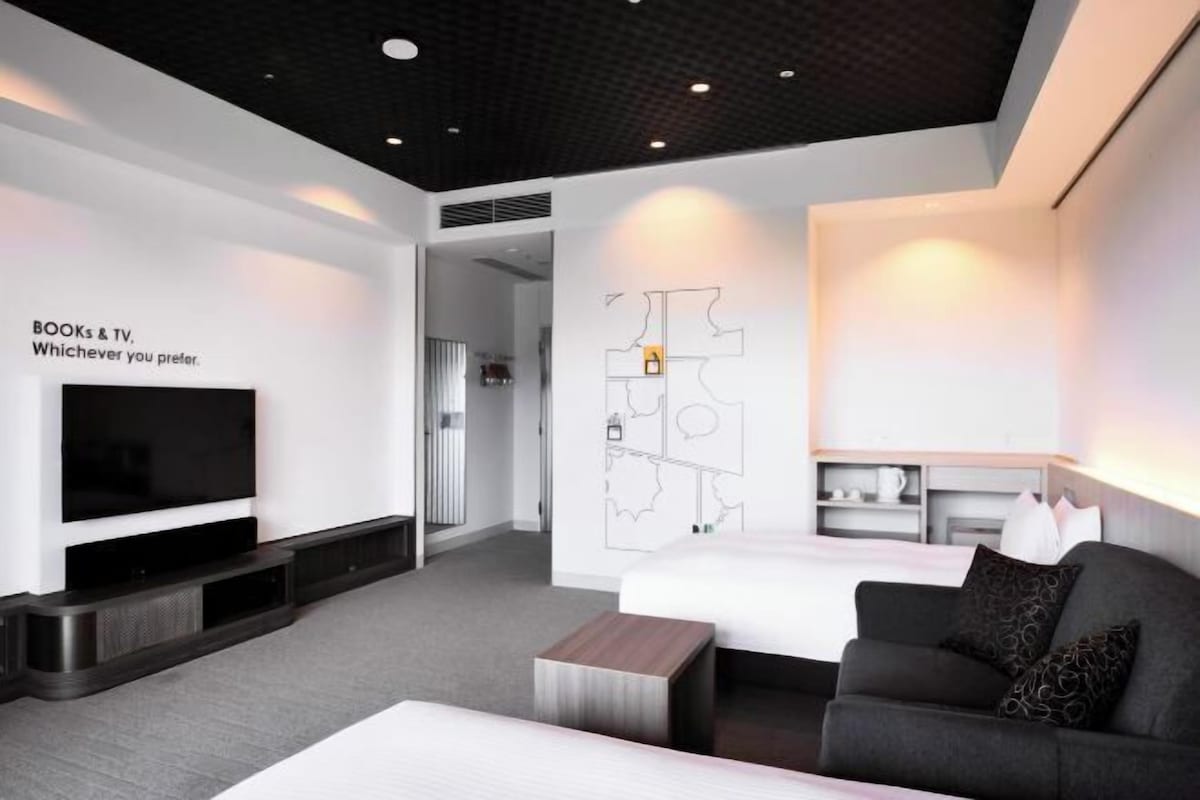 A modern hotel room with a flat-screen TV, a map on the wall, a sofa, and a coffee table.