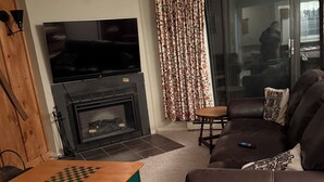 Una sala de estar con chimenea, televisor, sofá y una mesa para jugar al ajedrez.