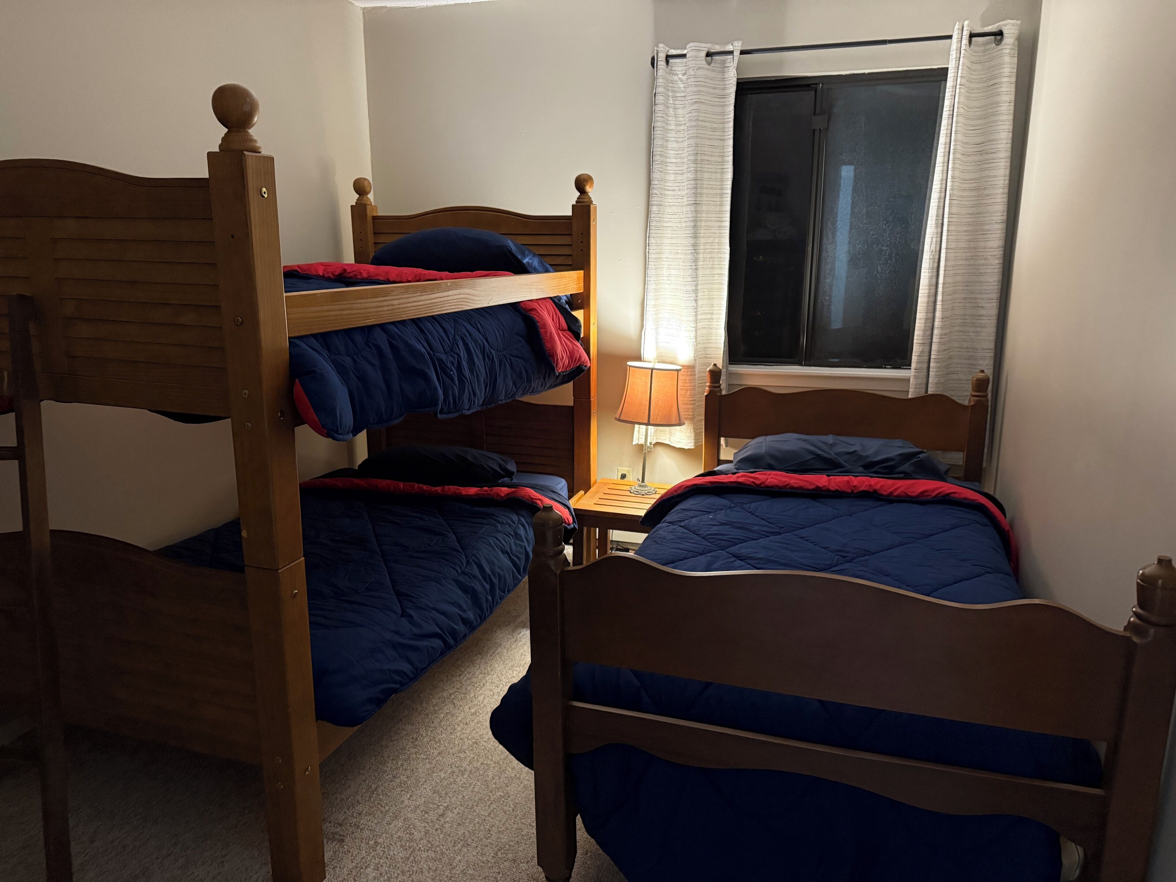 A bunk bed room with a window, a nightstand, and a lamp.