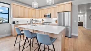 Una cucina moderna con mobili in legno, elettrodomestici in acciaio inossidabile e un'isola centrale con sgabelli da bar.