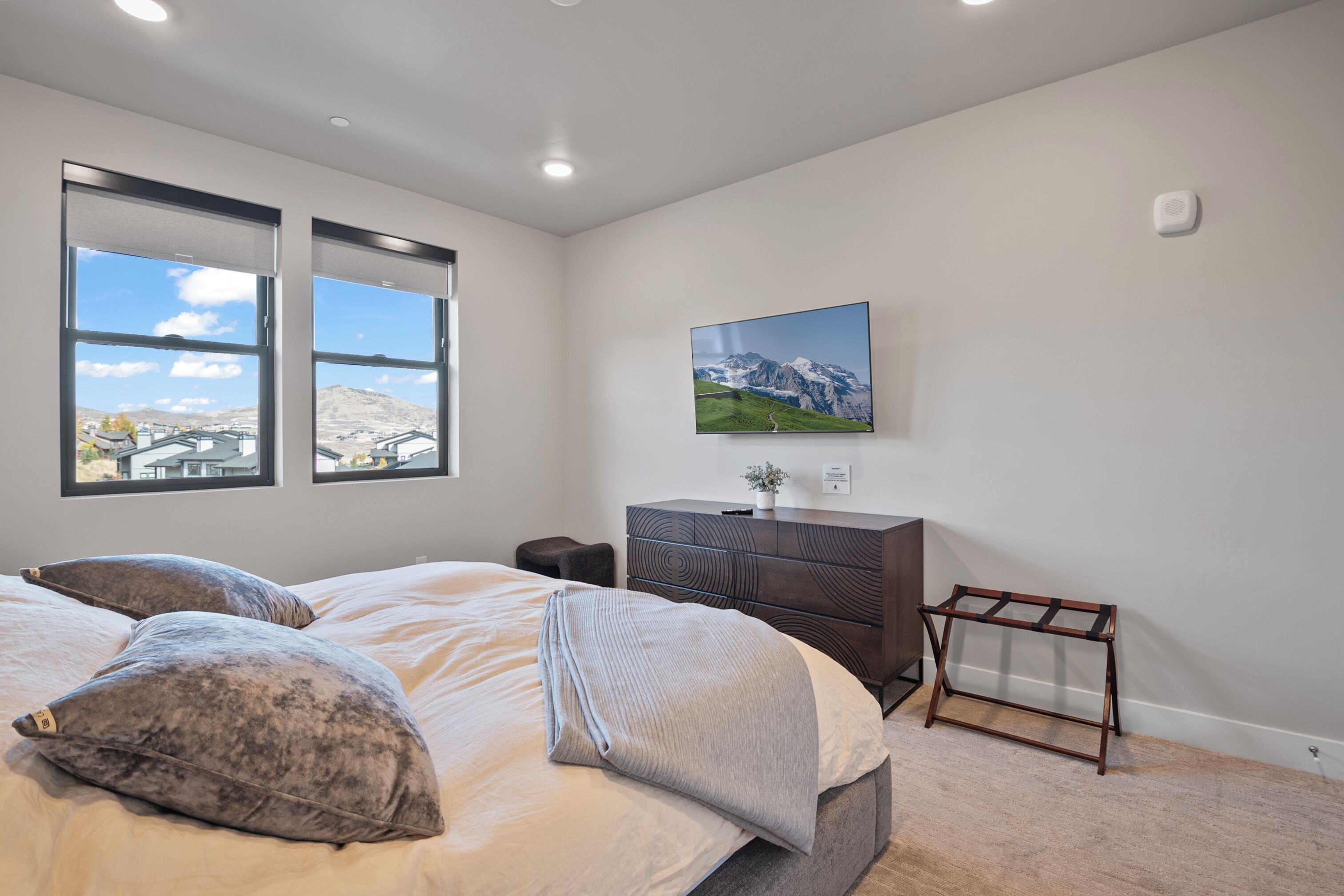 Une chambre à coucher avec un lit, des oreillers, une commode, une petite table et une fenêtre donnant sur la montagne.