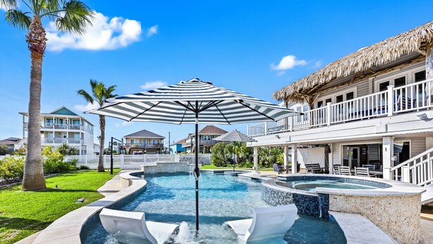 Una piscina con idromassaggio, circondata da una recinzione bianca, palme e una casa con tetto di paglia.
