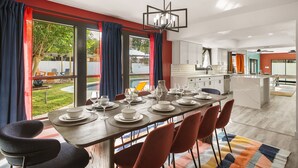 Un comedor moderno con una mesa grande dispuesta para seis personas, una cocina al fondo y vistas al exterior.