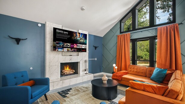 Una sala de estar moderna con chimenea, muebles azul y naranja, y un televisor montado en la pared.