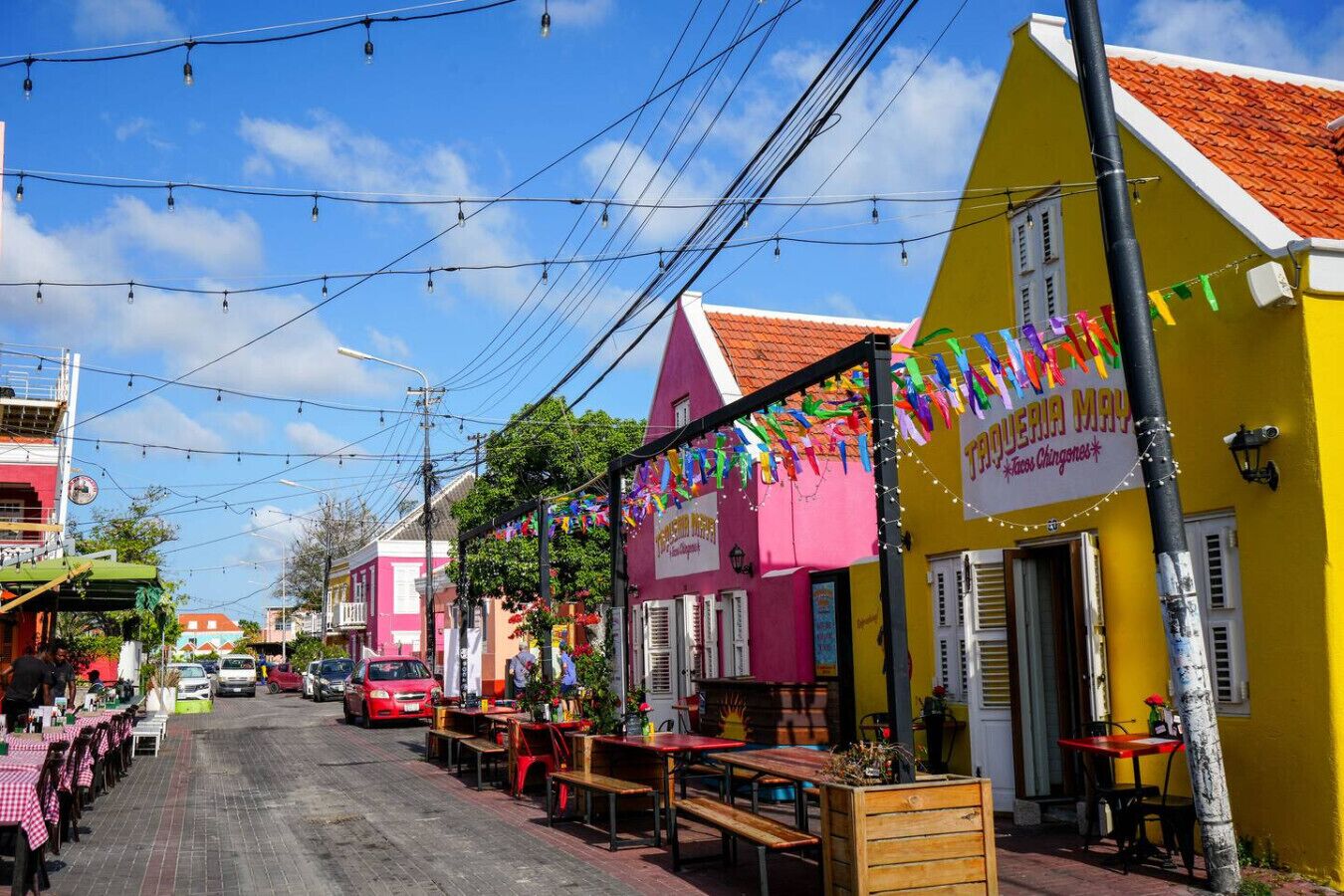 Una calle bordeada de edificios coloridos, con mesas al aire libre y guirnaldas de luces.