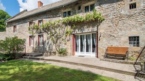 Un bâtiment en pierre avec un banc en bois, une porte et un petit espace aménagé en jardin.