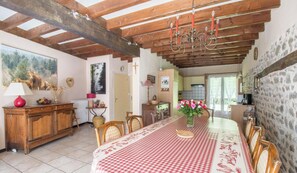 Un coin repas avec une nappe Ă carreaux, des chaises en bois, un lustre et une cuisine en arriĂšre-plan.