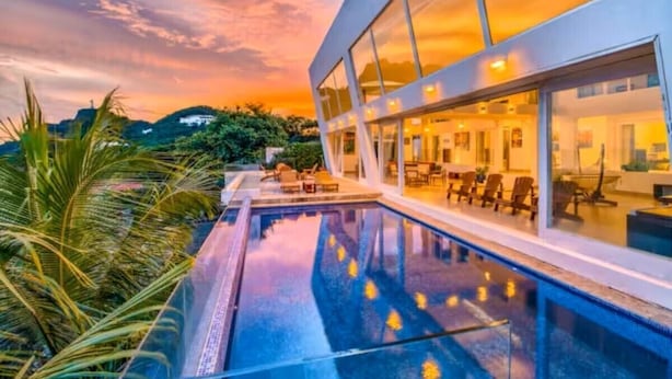 A modern building with a large glass facade, a swimming pool, and outdoor seating.