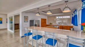 A modern kitchen with a central island, bar stools, pendant lighting, and a view into the dining area.