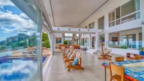 A modern hotel lobby with a pool, sun loungers, and a dining area.