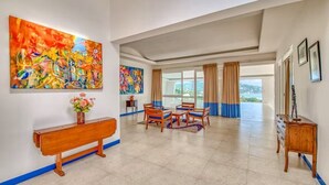 A spacious room with a large window, a wooden bench, a dining table with chairs, and two paintings on the walls.