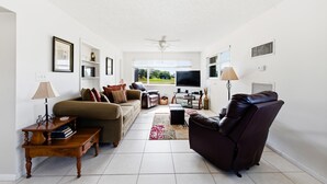 Una sala de estar con sofá, sillón, televisión y ventilador de techo.