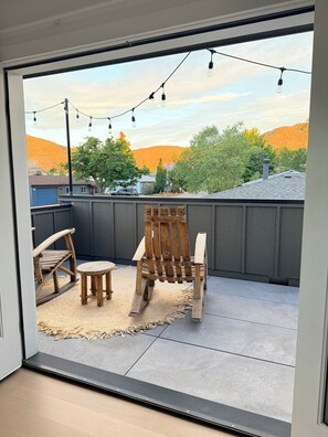 A wooden deck with a chair and table, a string of lights, and a view of a hilly landscape.