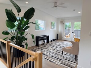 A spacious room with a piano, a large plant, and a view of the outdoors through a sliding glass door.