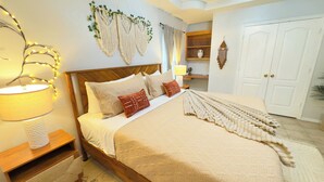 Un dormitorio ordenado con cama, lámparas de noche, un colgador de macramé y una puerta.