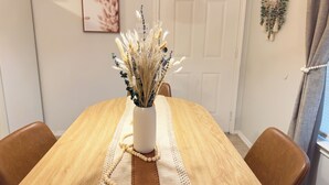 Una mesa de comedor con un jarrón blanco que contiene flores secas, rodeada de sillas de cuero marrón.