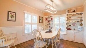 A dining area with a white table and chairs, a chandelier, and shelves with dishes and decorations. - Vintage Rodeo style home in historic Downtown Weatherford TX. (Weatherford)