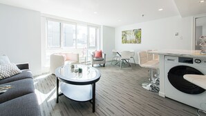 Un salon moderne avec un canapé gris, une table basse ronde, un lave-linge et un coin repas comprenant des chaises et une table.