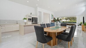 Une cuisine moderne avec des meubles blancs, un îlot central et un coin repas comprenant une table en bois et des chaises à revêtement gris.