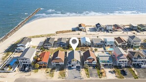 Vue aérienne d’une zone résidentielle côtière, avec des maisons, une plage et une jetée.
